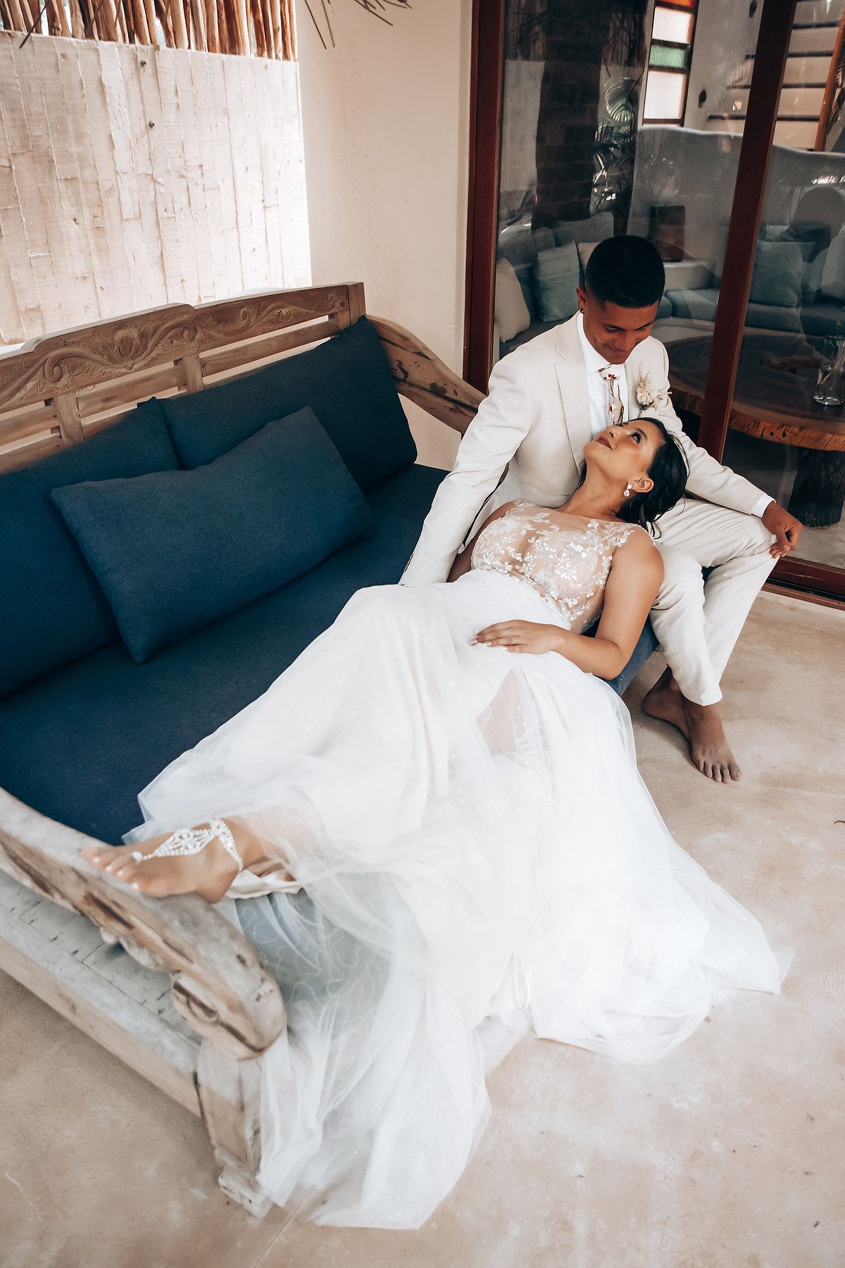 A couple in wedding attire lounges together on a gray couch during an intimate moment.