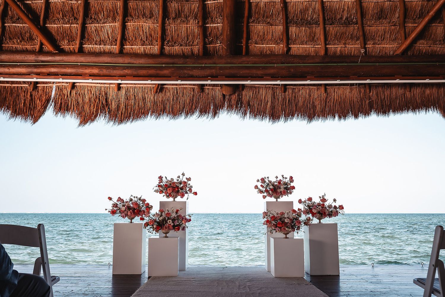 Beachfront wedding ceremony setup under thatched palm roof with ocean views.