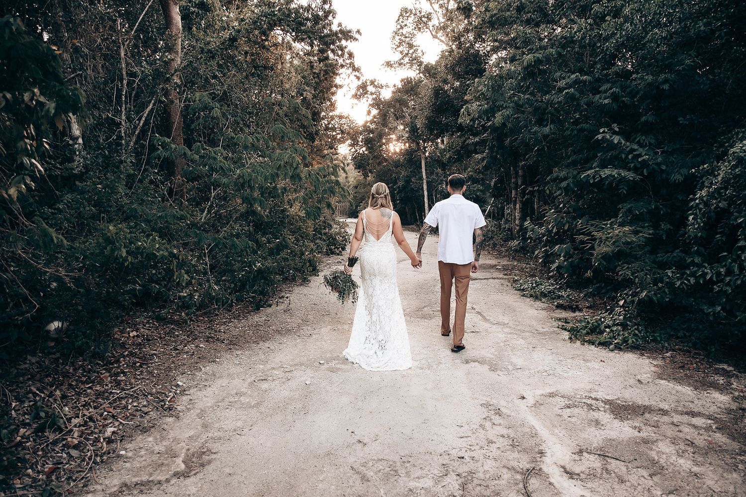 Dirt path through forest with white-clad figures walking away from camera.