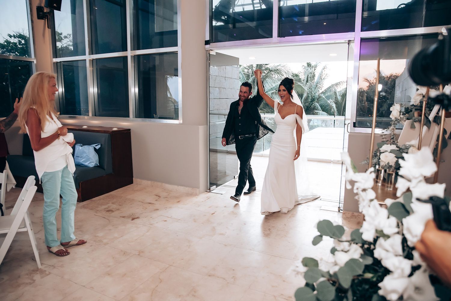 Wedding party dancing and celebrating in an elegant indoor venue with white decor.