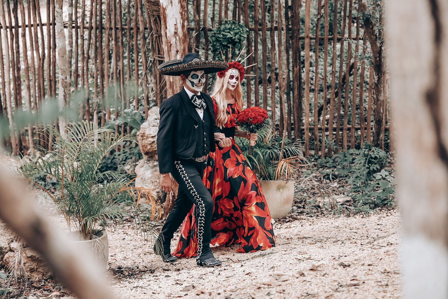 A couple in Day of the Dead themed attire poses in a forest setting.