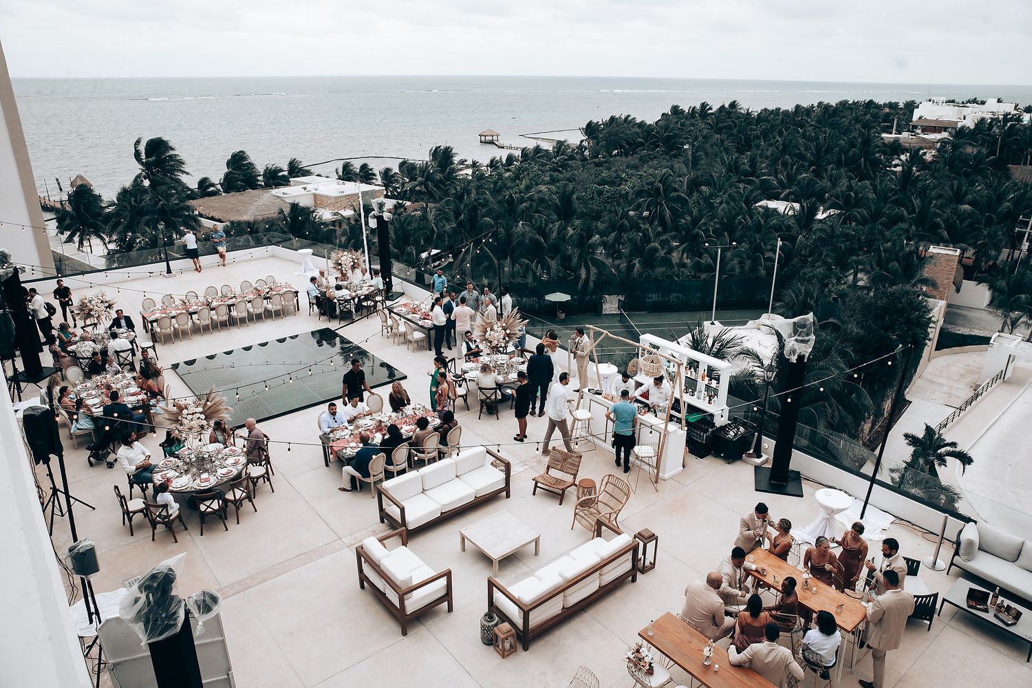 Aerial view of an outdoor wedding reception with long tables and wooden chairs.