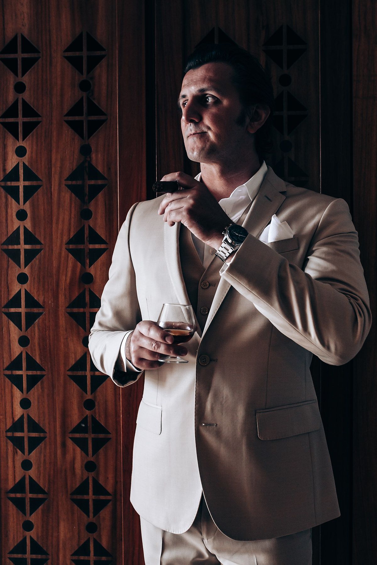 Groomsmen in light colored suits enjoying drinks during wedding preparations.