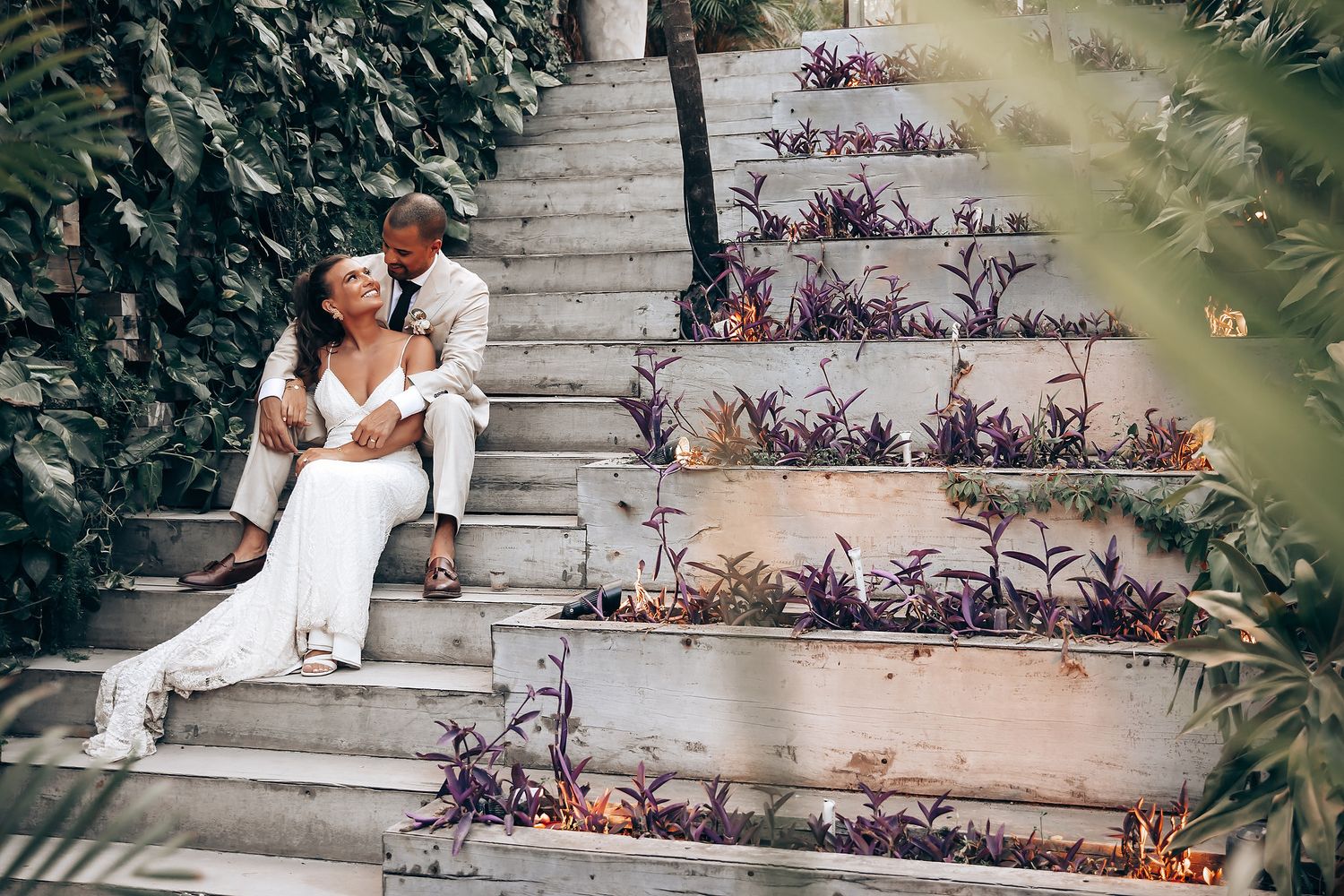Couple shares intimate moment on stone steps surrounded by purple flowers and greenery.