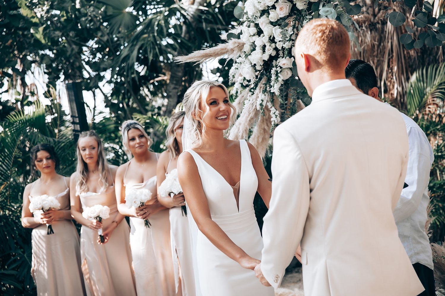 Wedding party in neutral colors gathered outdoors for ceremony photos.