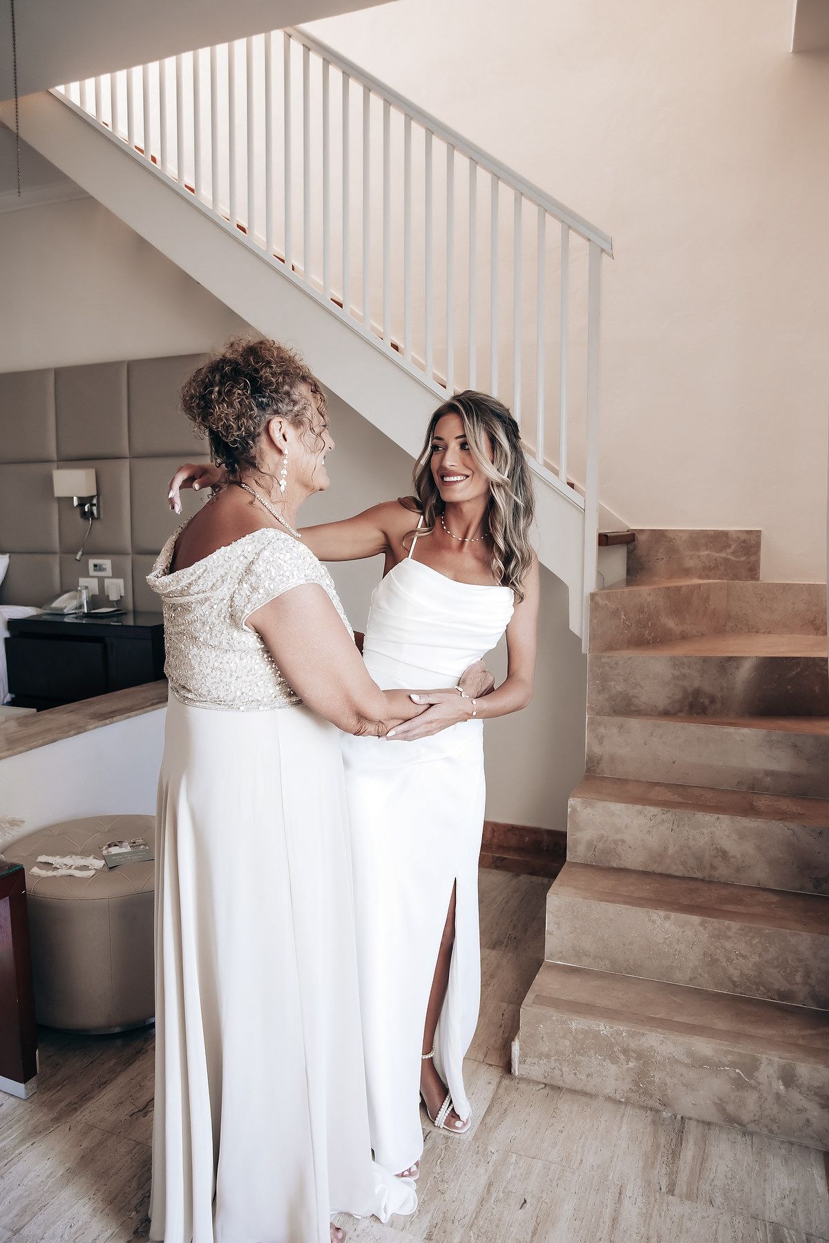 An image of two women in white wedding dresses embracing on a staircase.