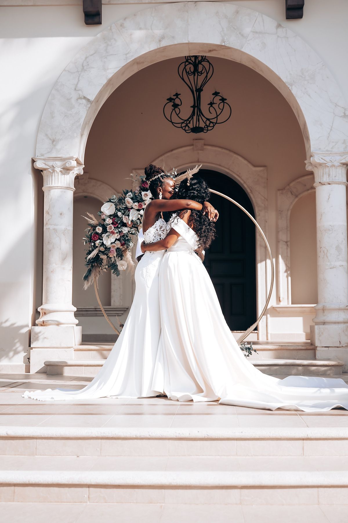 Wedding party posing under white stone archways with decorative lighting.