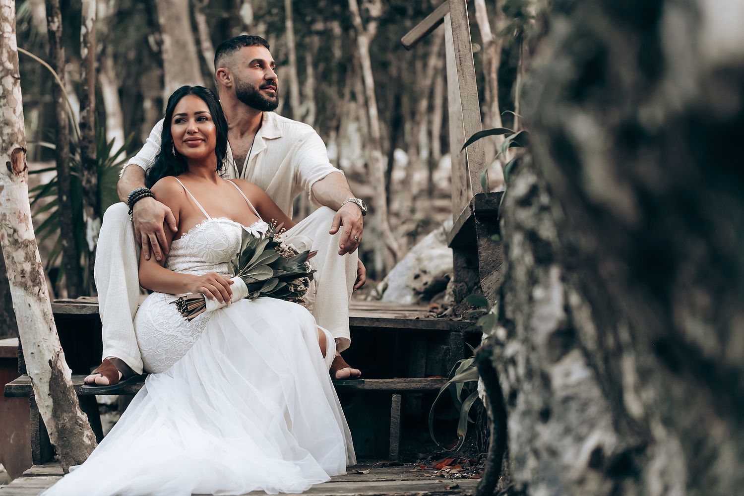 Romantic forest wedding scene with couple seated among natural woodland surroundings.