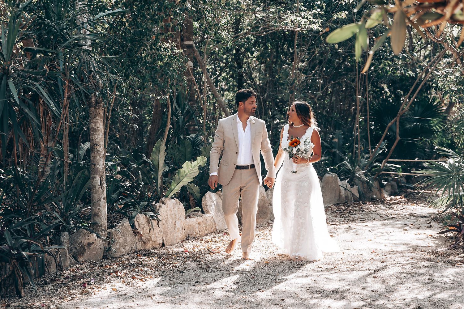 Wedding party walking through a sunlit forest path in formal attire.