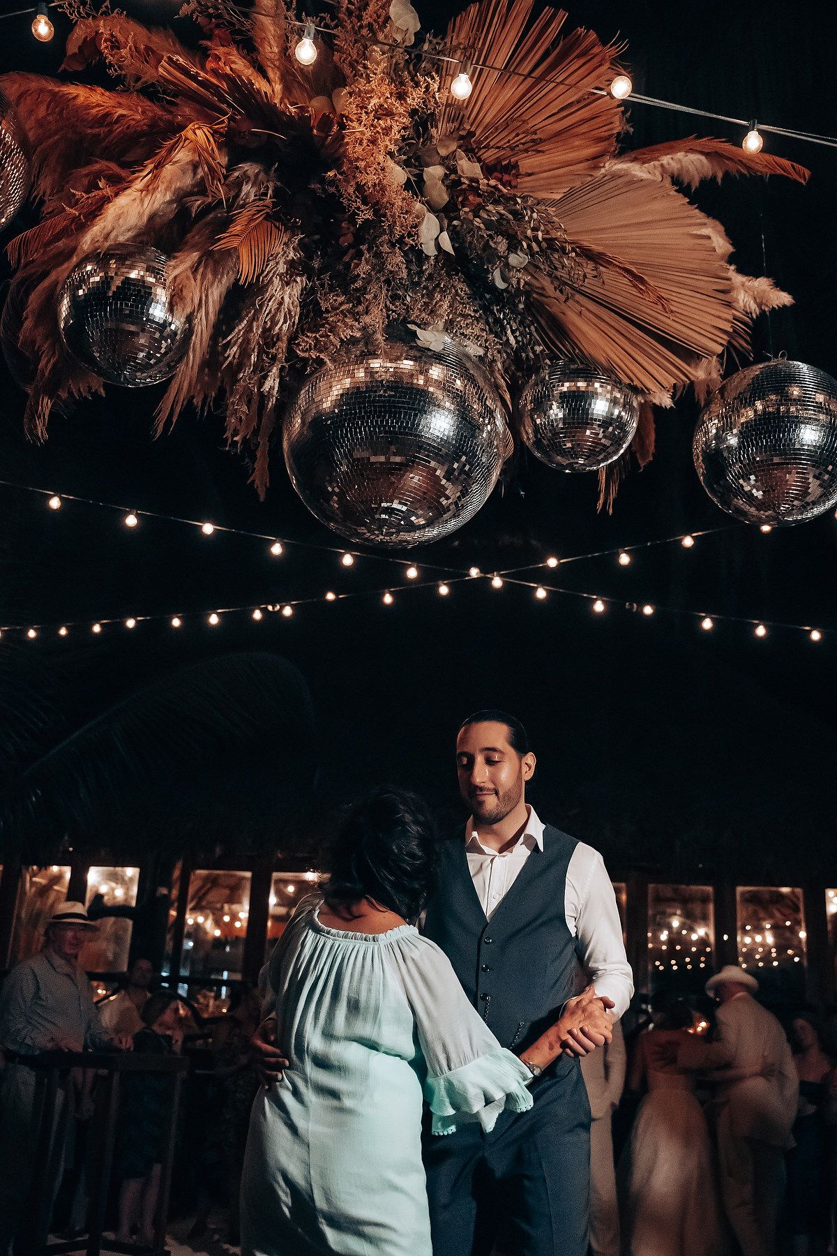Wedding reception venue decorated with dried palm fronds and string lights overhead.