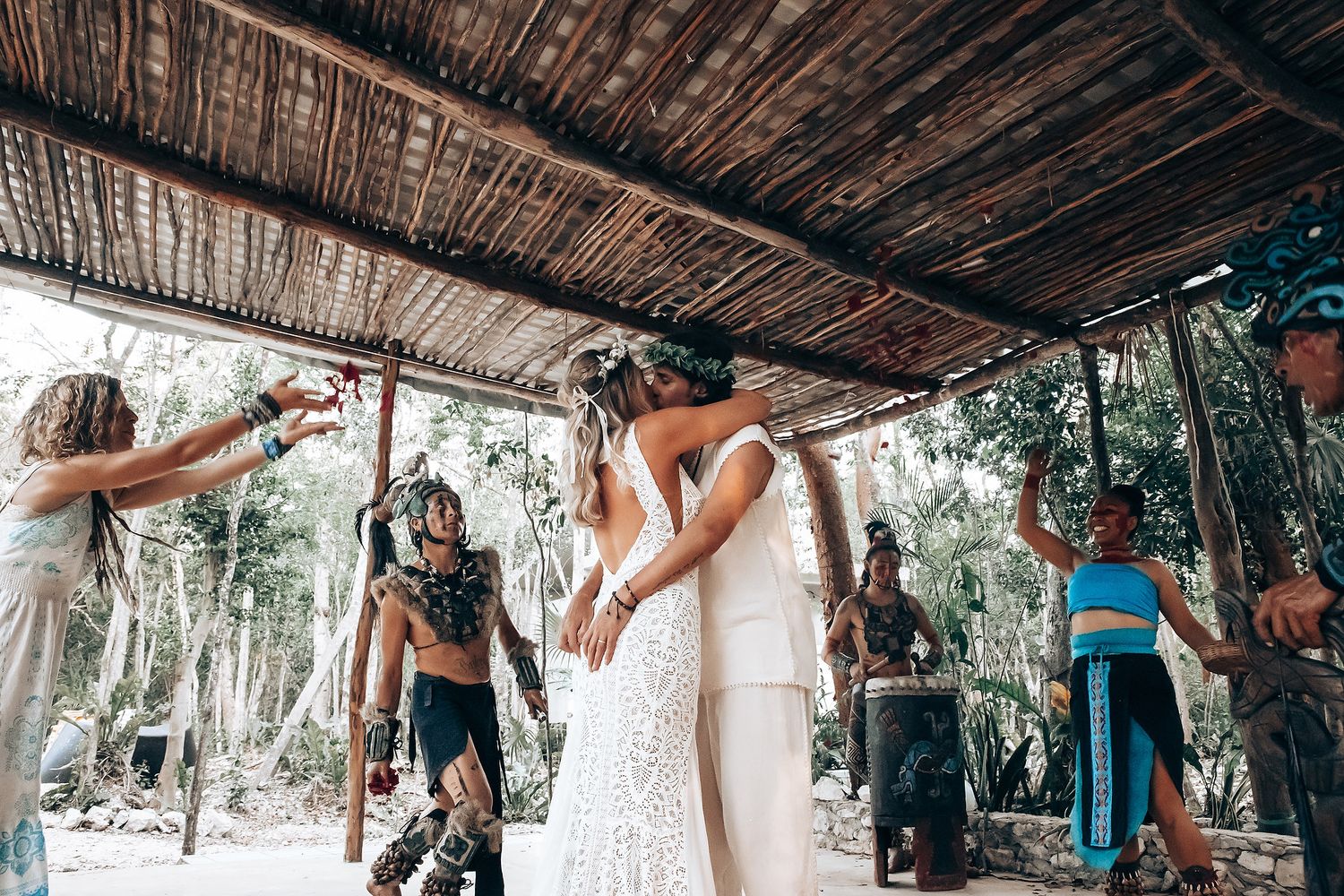 People dancing and celebrating under a rustic wooden shelter in an outdoor setting during a festive gathering.