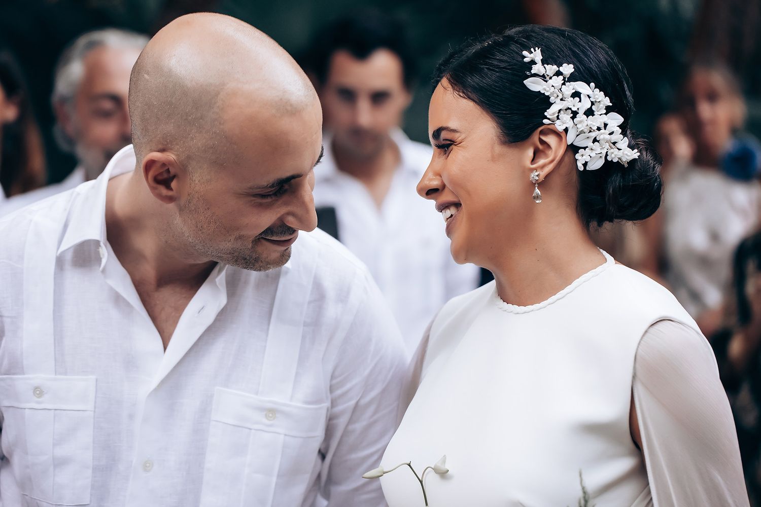 A romantic wedding moment showing a couple in white attire sharing a joyful look with the bride wearing an elegant hair accessory.