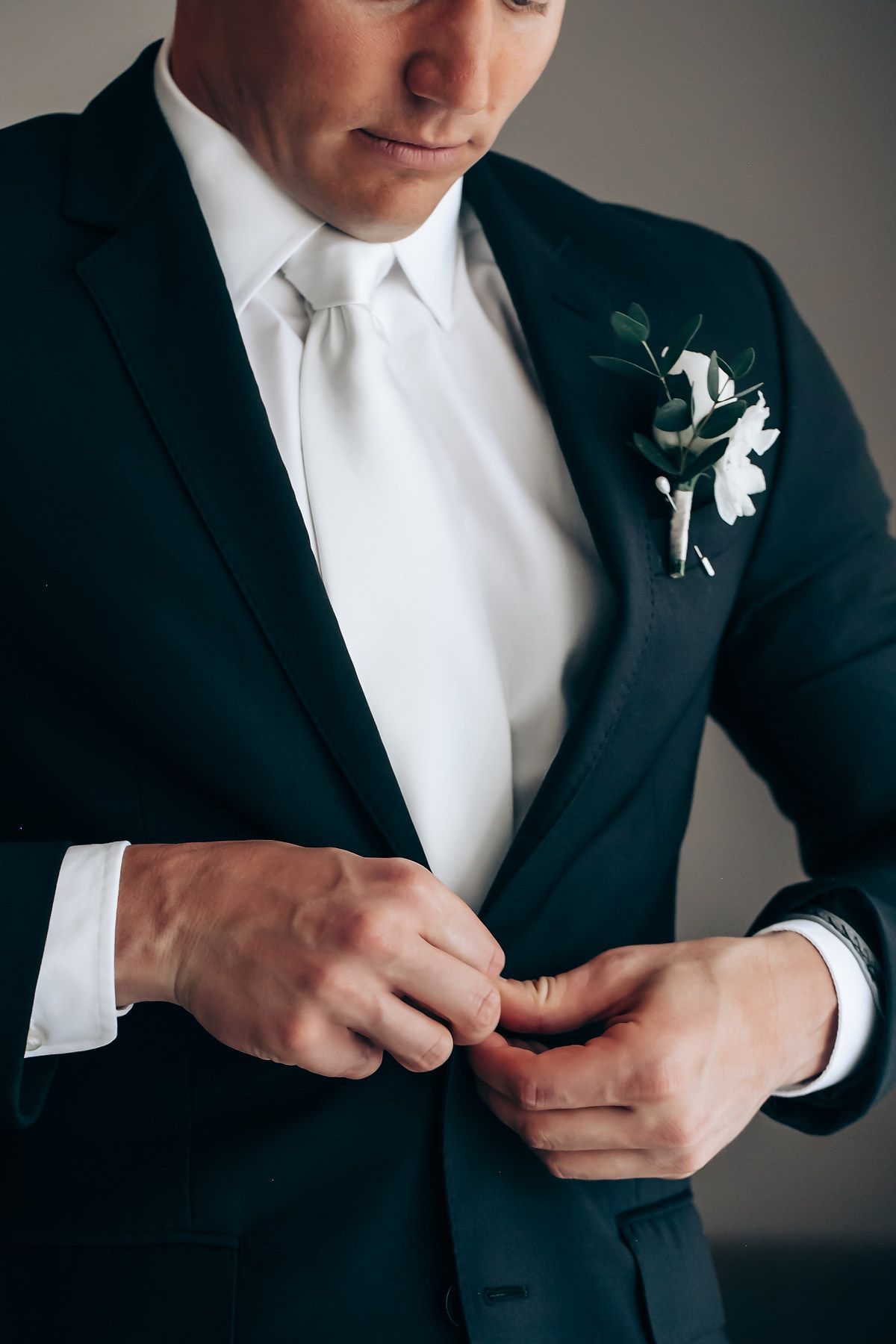 Detail shots of a groom's formal attire showing black suit jacket with white boutonniere.