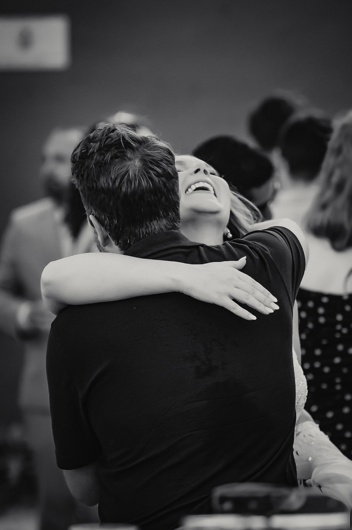 Black and white photo of woman laughing while embracing partner at wedding reception.