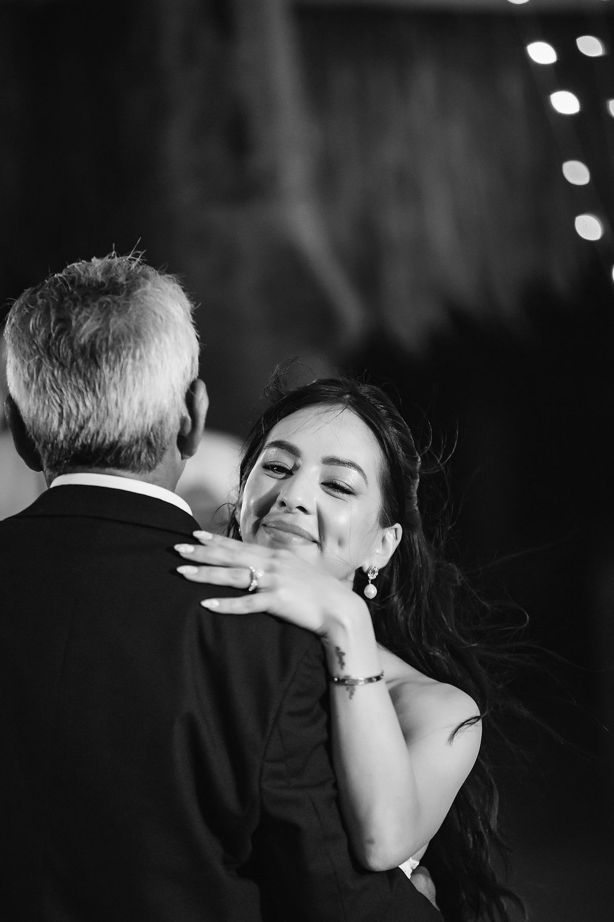 Black and white photo of a bride sharing an emotional father-daughter dance, smiling warmly at her partner.