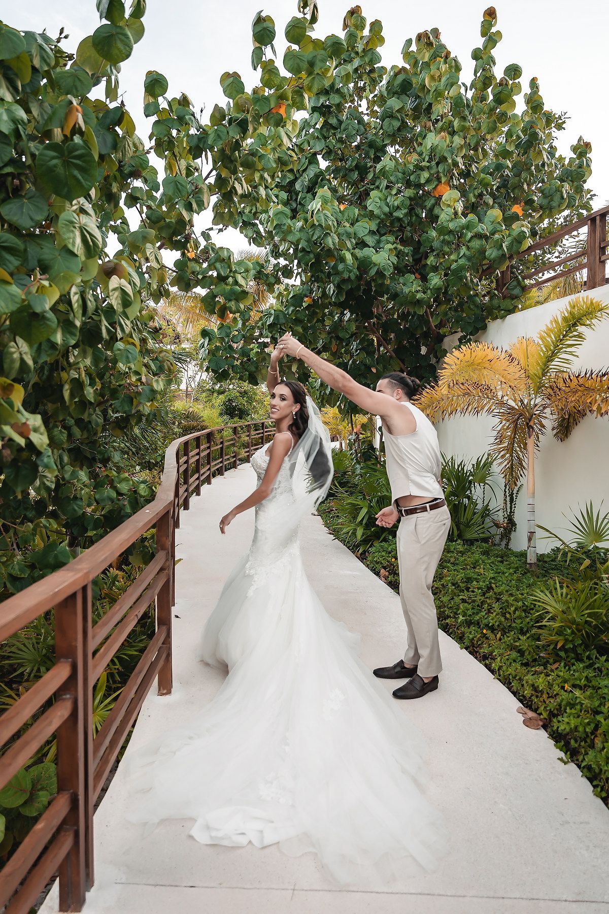 Bride and groom dancing on a white pathway surrounded by lush tropical greenery at an outdoor wedding venue.
