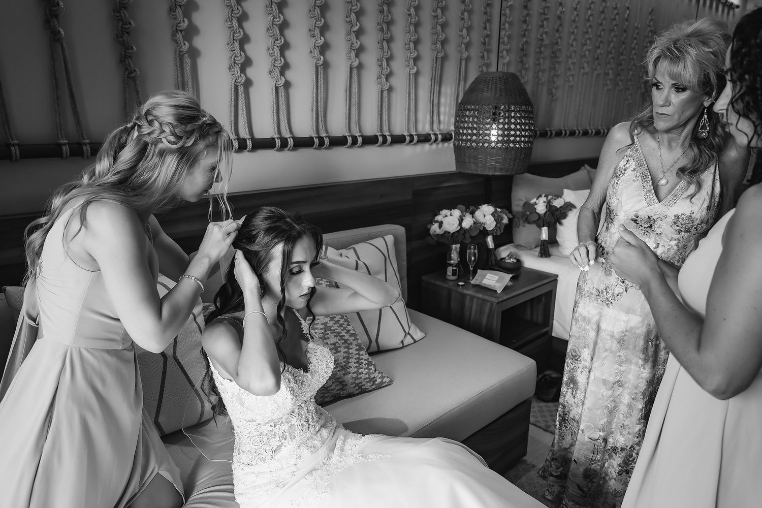 Bridesmaids help a bride with her hair and accessories in a candid black and white wedding preparation photo.