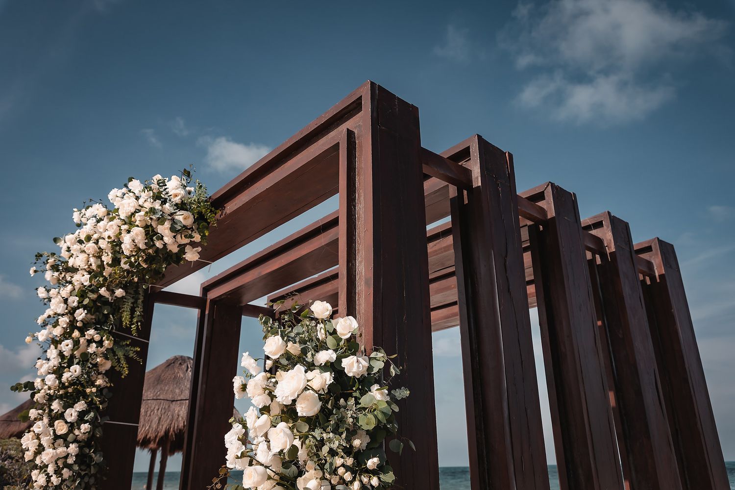 Elegant outdoor wedding arch with dark wood frames adorned with white floral arrangements against a blue sky.