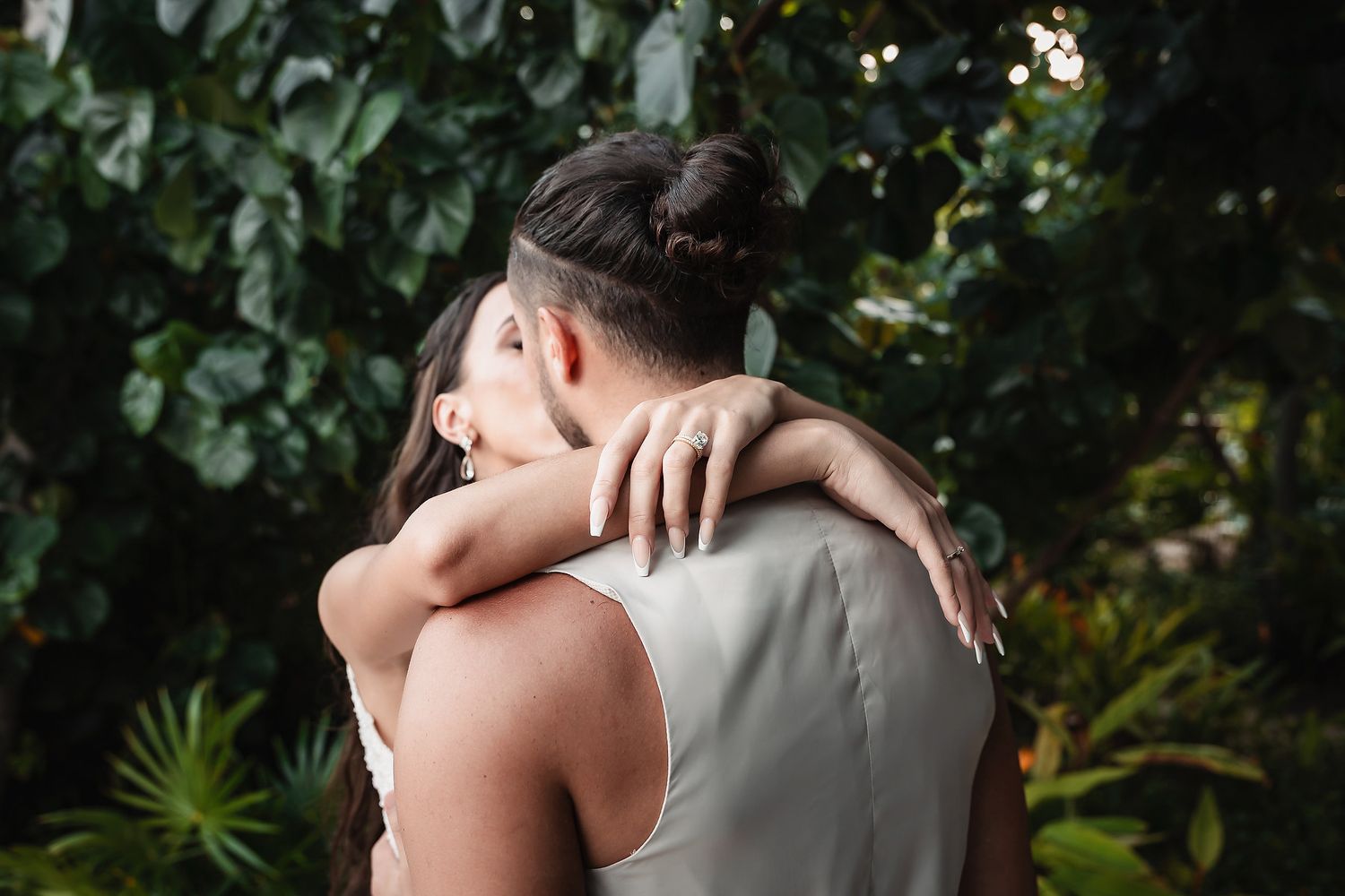 Couple embracing romantically in a lush tropical garden, sharing an intimate moment surrounded by green foliage.