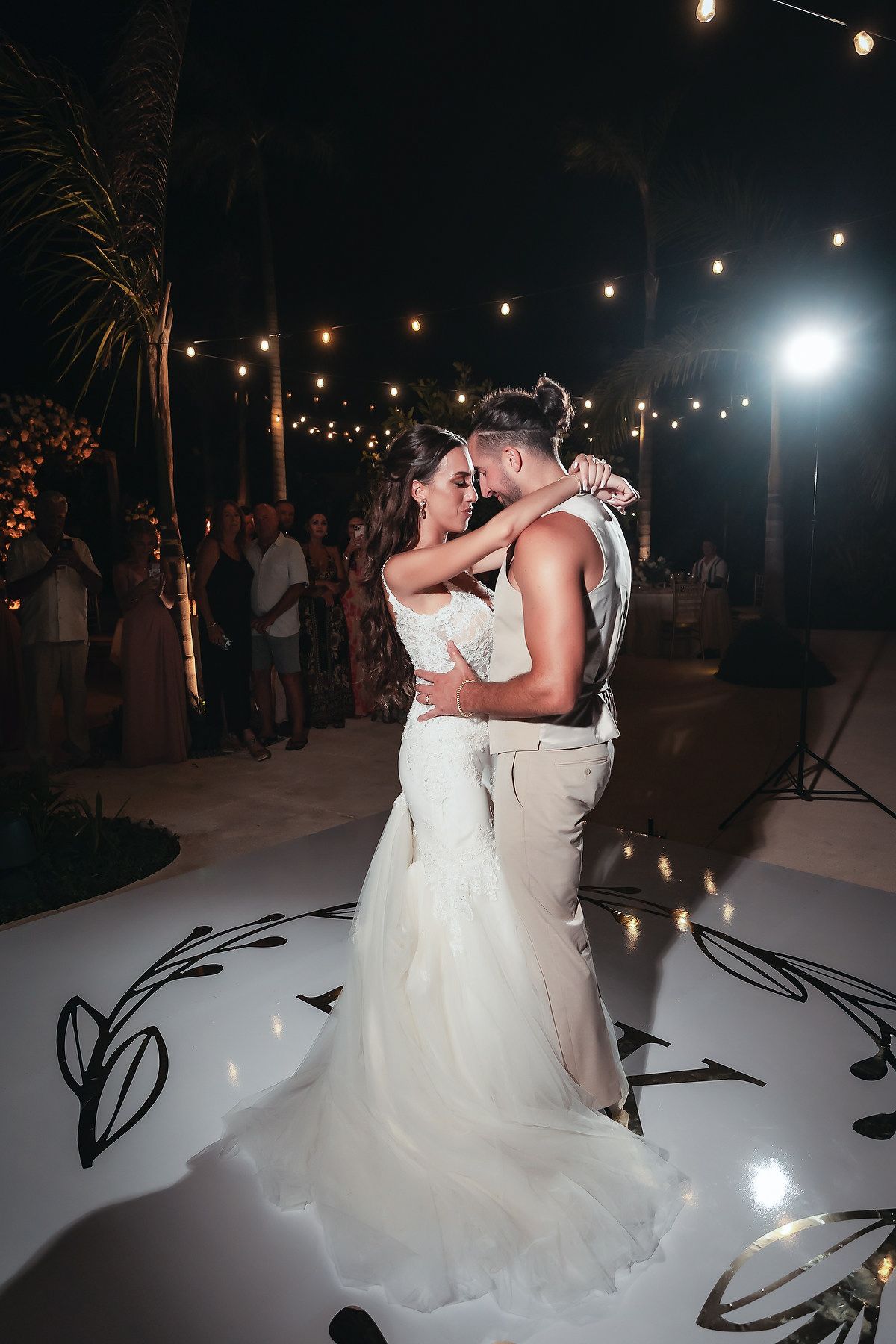 Bride and groom share romantic first dance under string lights at outdoor wedding reception at night.
