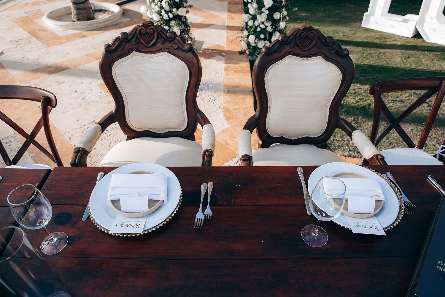 A rustic dining table setup with elegant place settings, wooden chairs, and decorative plates in a natural outdoor setting.