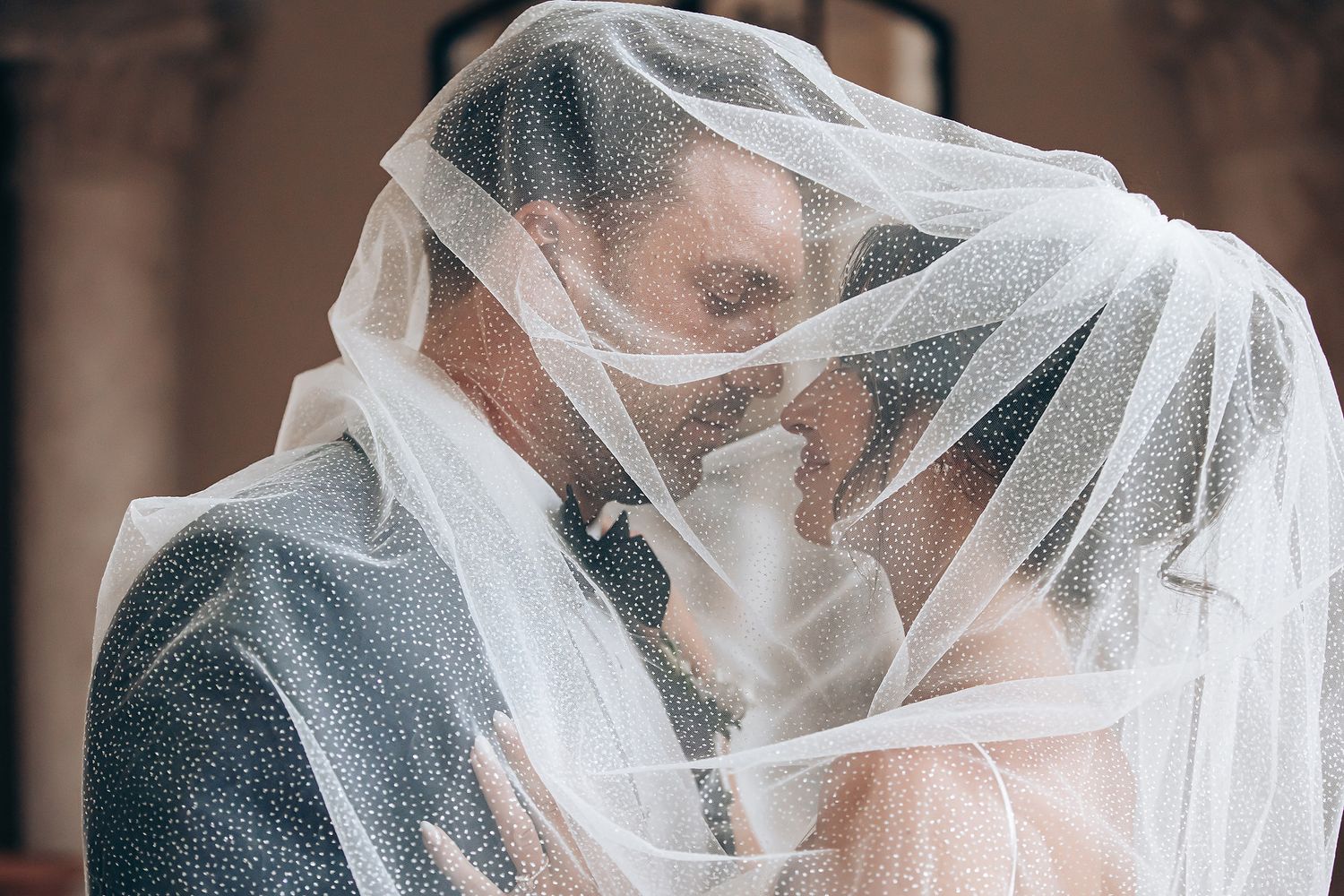Romantic wedding moment captured through delicate white veil as couple shares intimate kiss.