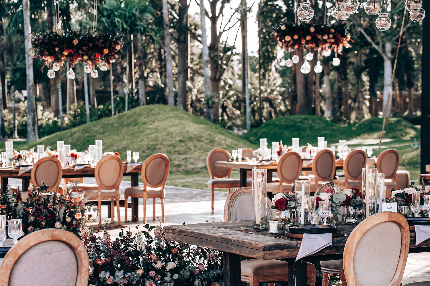 Elegant outdoor wedding reception setup with brown chairs and tables under trees with string lights and floral decor.