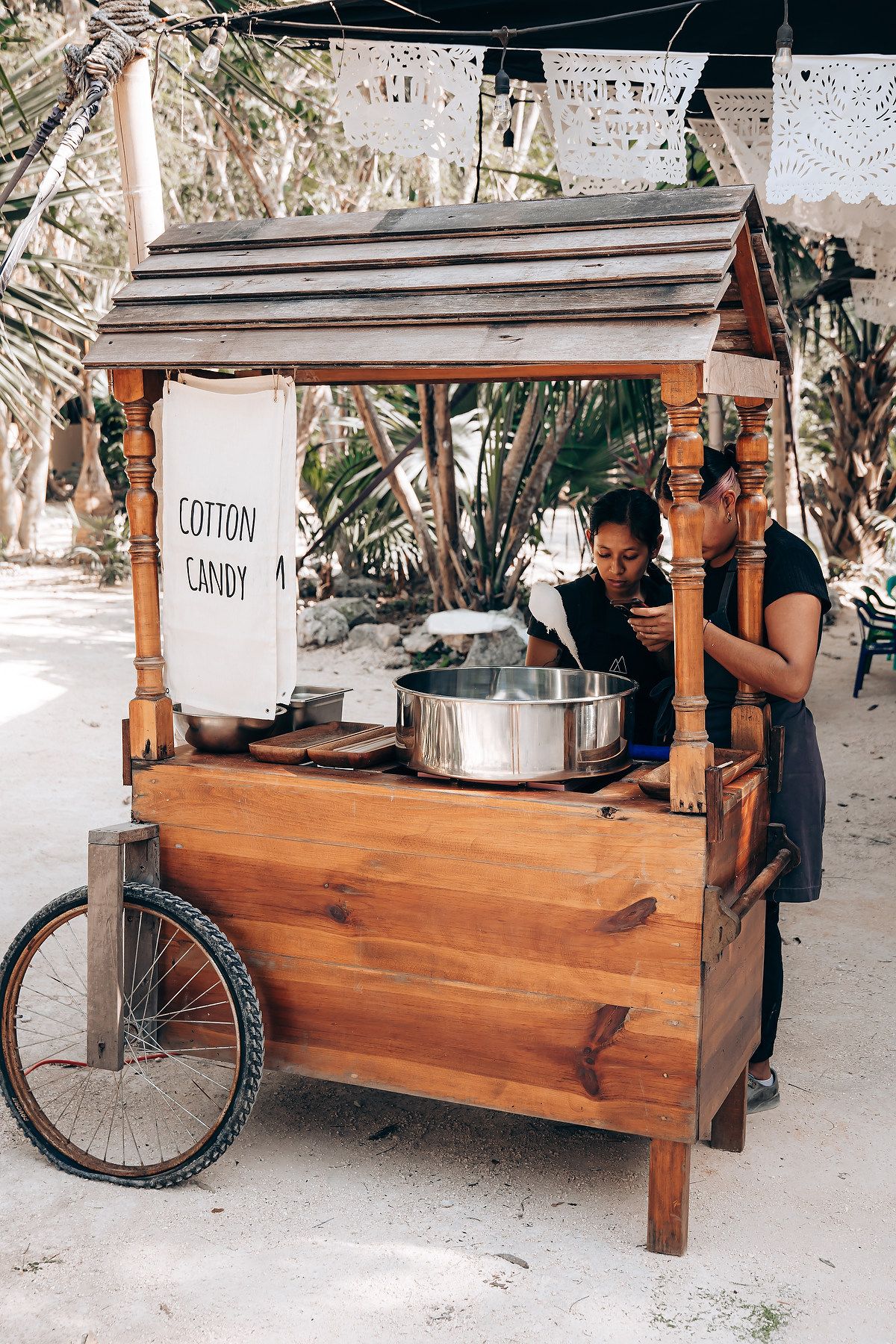 Rustic wooden mobile bar cart with wheels and storage compartments set up at an outdoor event.