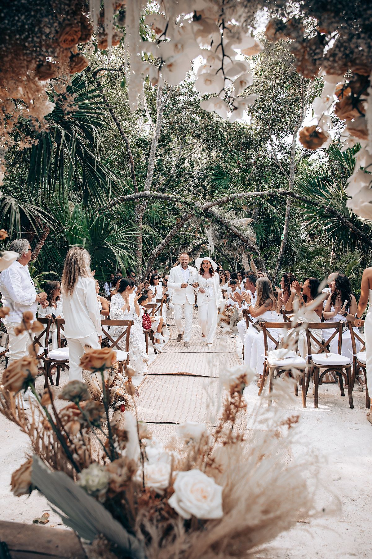 Outdoor wedding ceremony setup with wooden chairs and tropical palm trees in a garden setting.