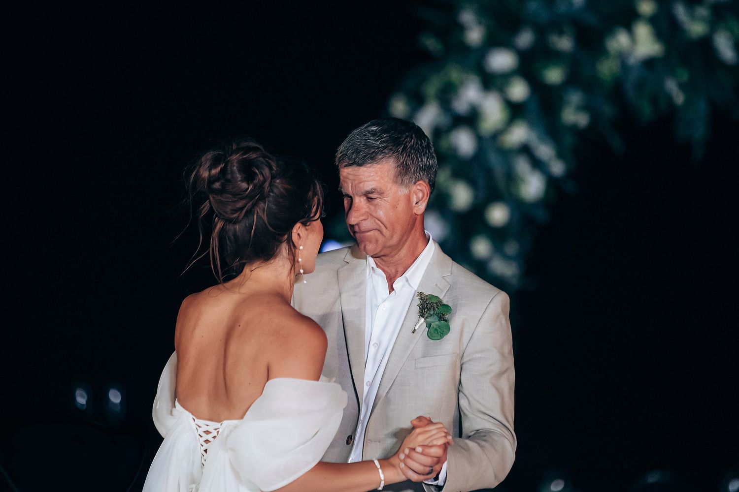 Couple shares an intimate dance in white attire against a dark background with soft lighting.