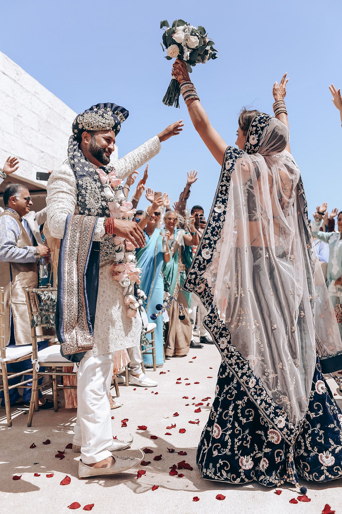 Wedding party in traditional attire celebrates on a sunny outdoor terrace.