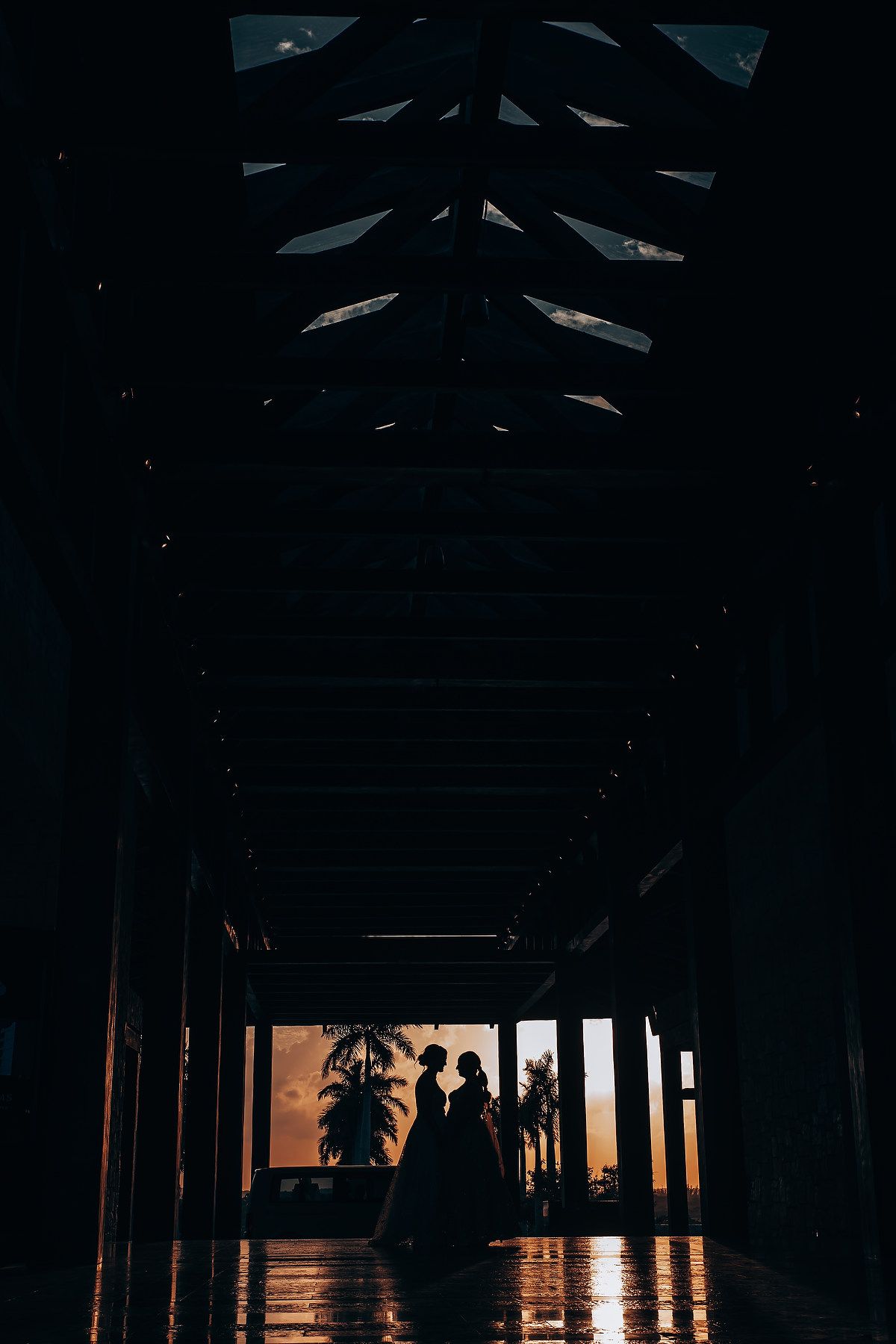 Dark silhouettes of pillars against a sunset sky viewed through a covered walkway.