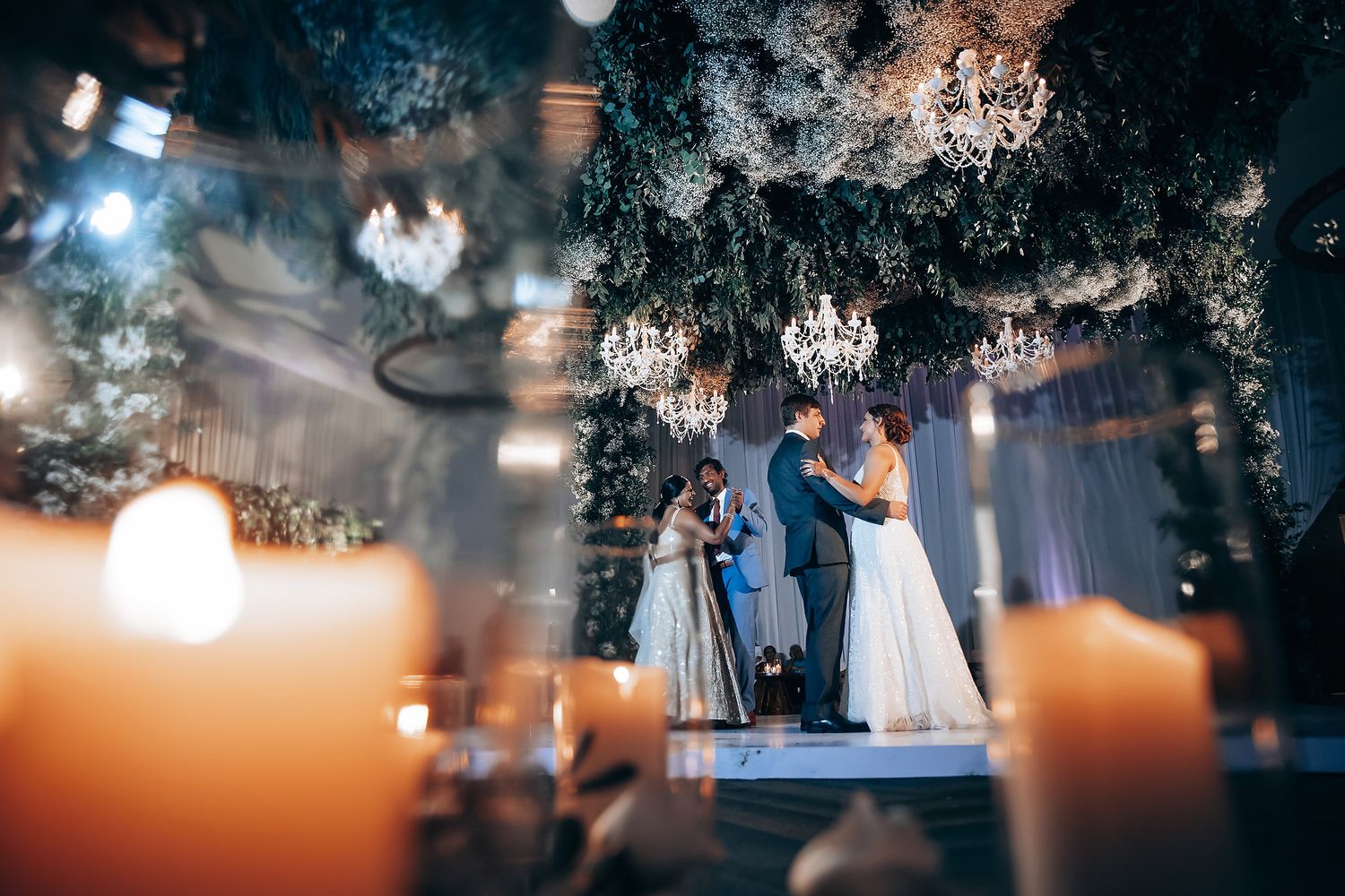 Atmospheric wedding venue illuminated by warm candlelight and hanging crystal chandeliers.
