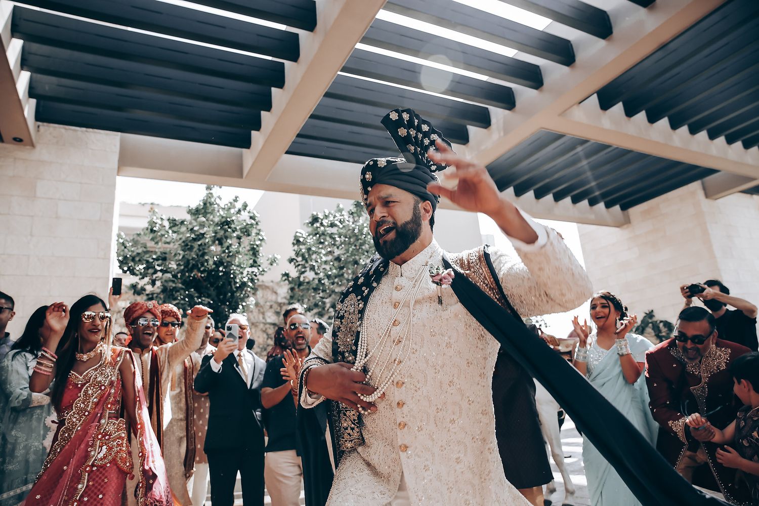 Wedding party dances energetically in formation beneath white beams and outdoor lighting.