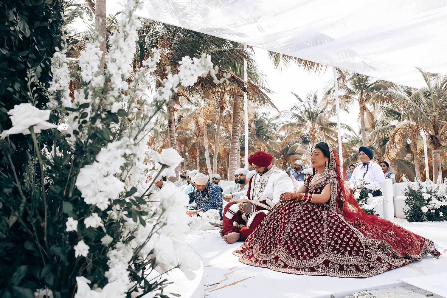 Beachfront wedding ceremony space decorated with white flowers and palm trees.