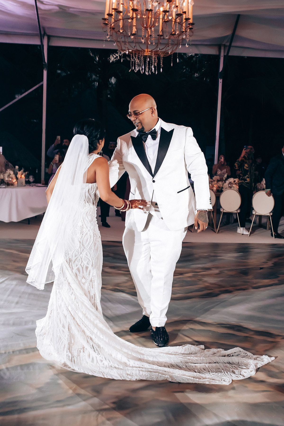 Elegant first dance moment under crystal chandeliers on a patterned dance floor.