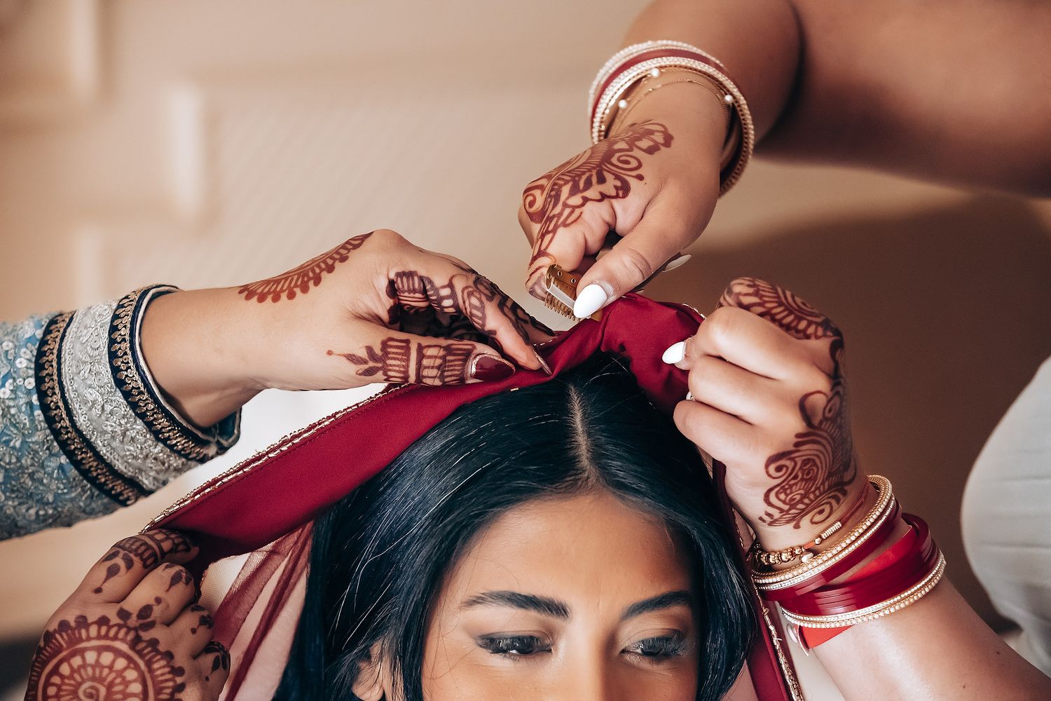 Hands placing red dupatta on bride wearing traditional Indian wedding attire and henna.