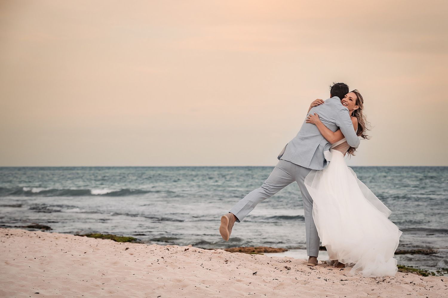 Couple in wedding attire shares intimate moments on a tropical beach at dusk.