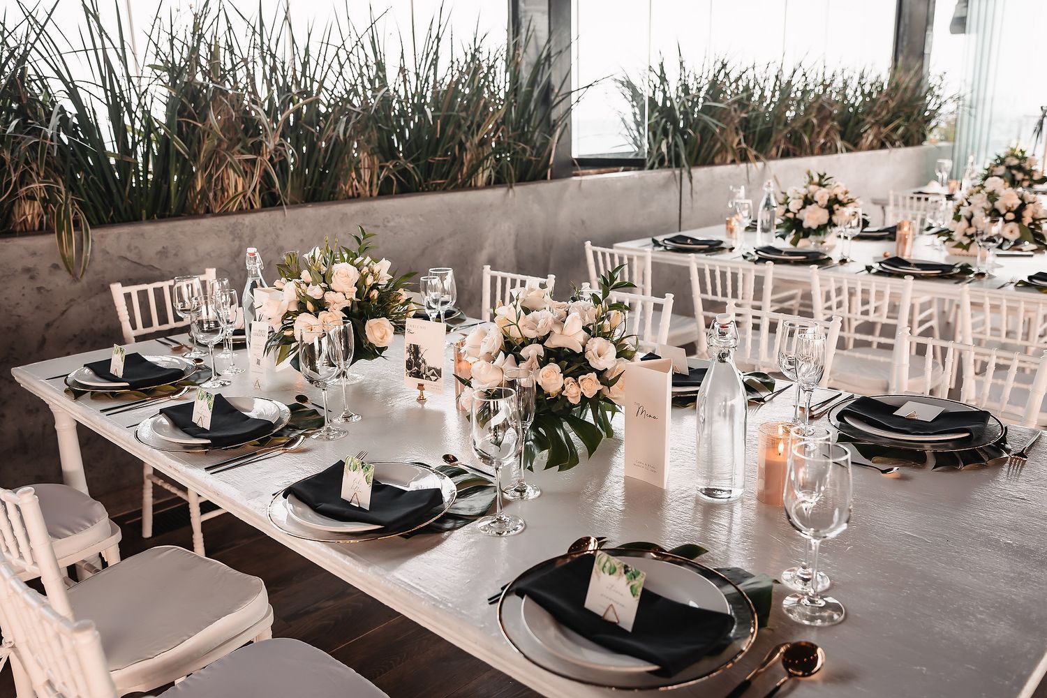 Long white dining tables set for wedding reception with white chairs and hanging woven decor.
