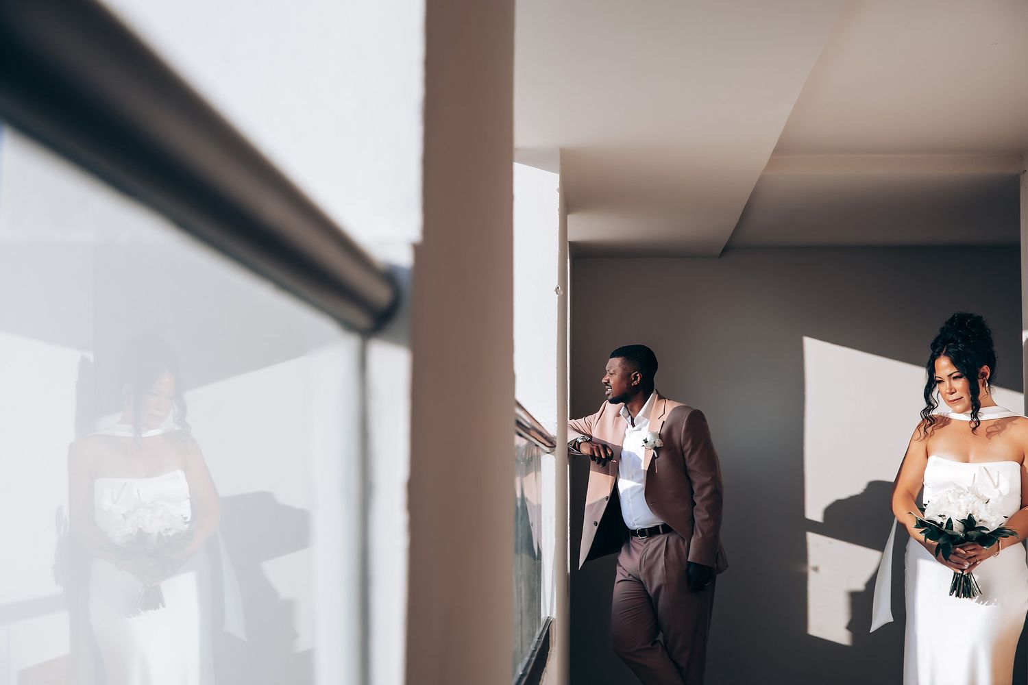 Wedding party members pose in bright indoor hallway with strong contrast lighting.