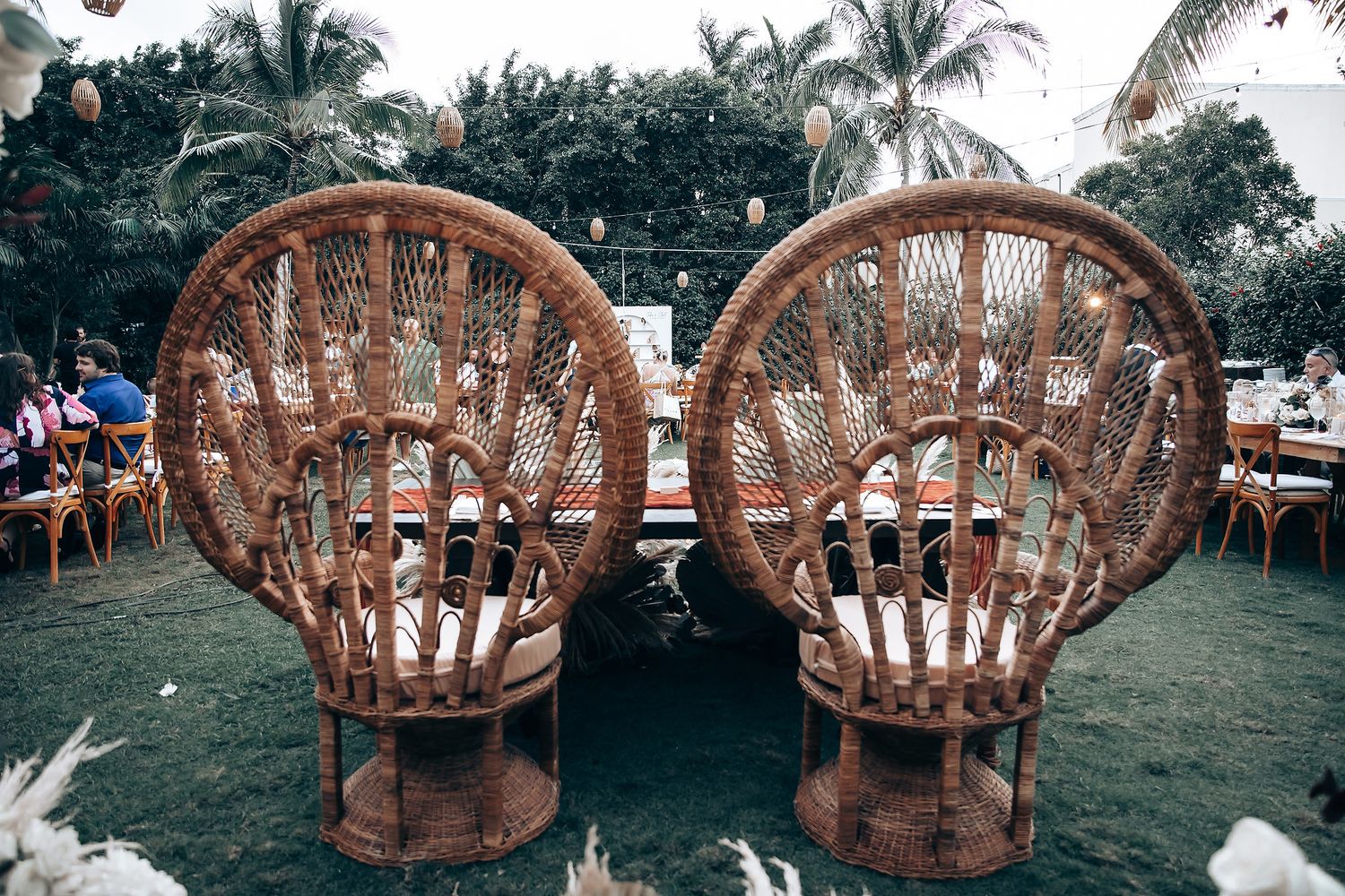 Tropical garden wedding setup with wooden peacock chairs and palm trees.