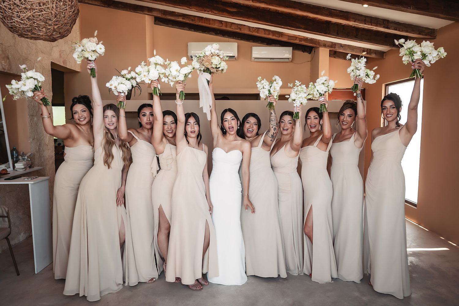 Bridesmaids in elegant cream-colored dresses lined up for a formal wedding party photo.