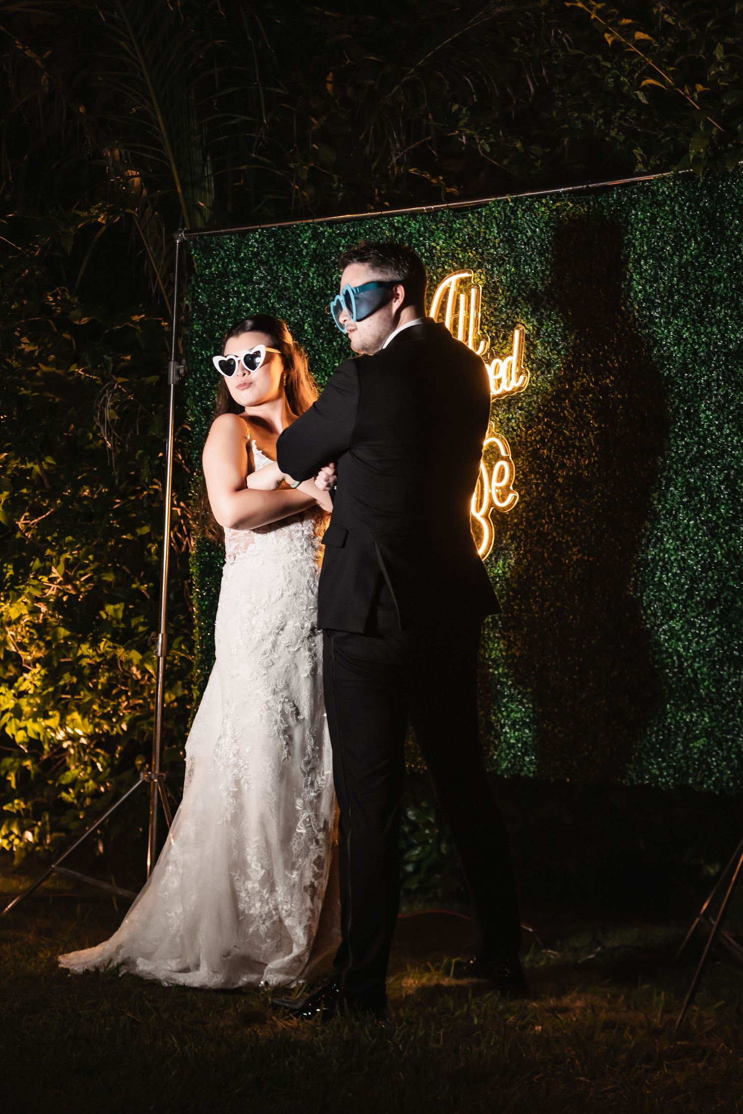 Wedding couple poses against a dark garden backdrop with dramatic lighting and ivy walls.