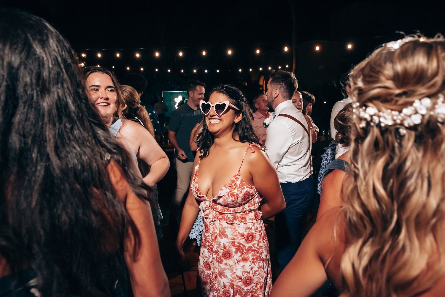 Lively wedding reception dance floor with guests celebrating under string lights.