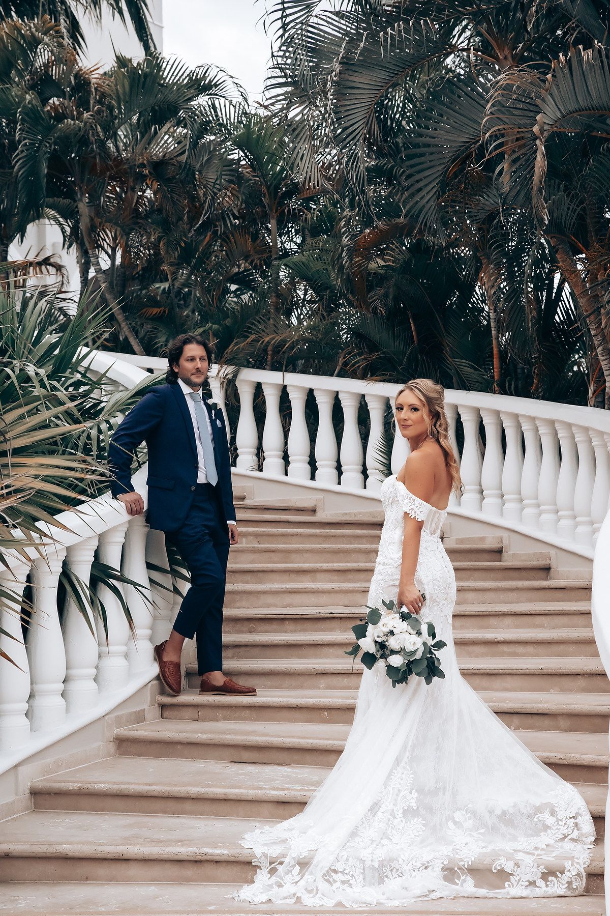 Elegant wedding photo shoot on grand white staircase surrounded by tropical palm trees.