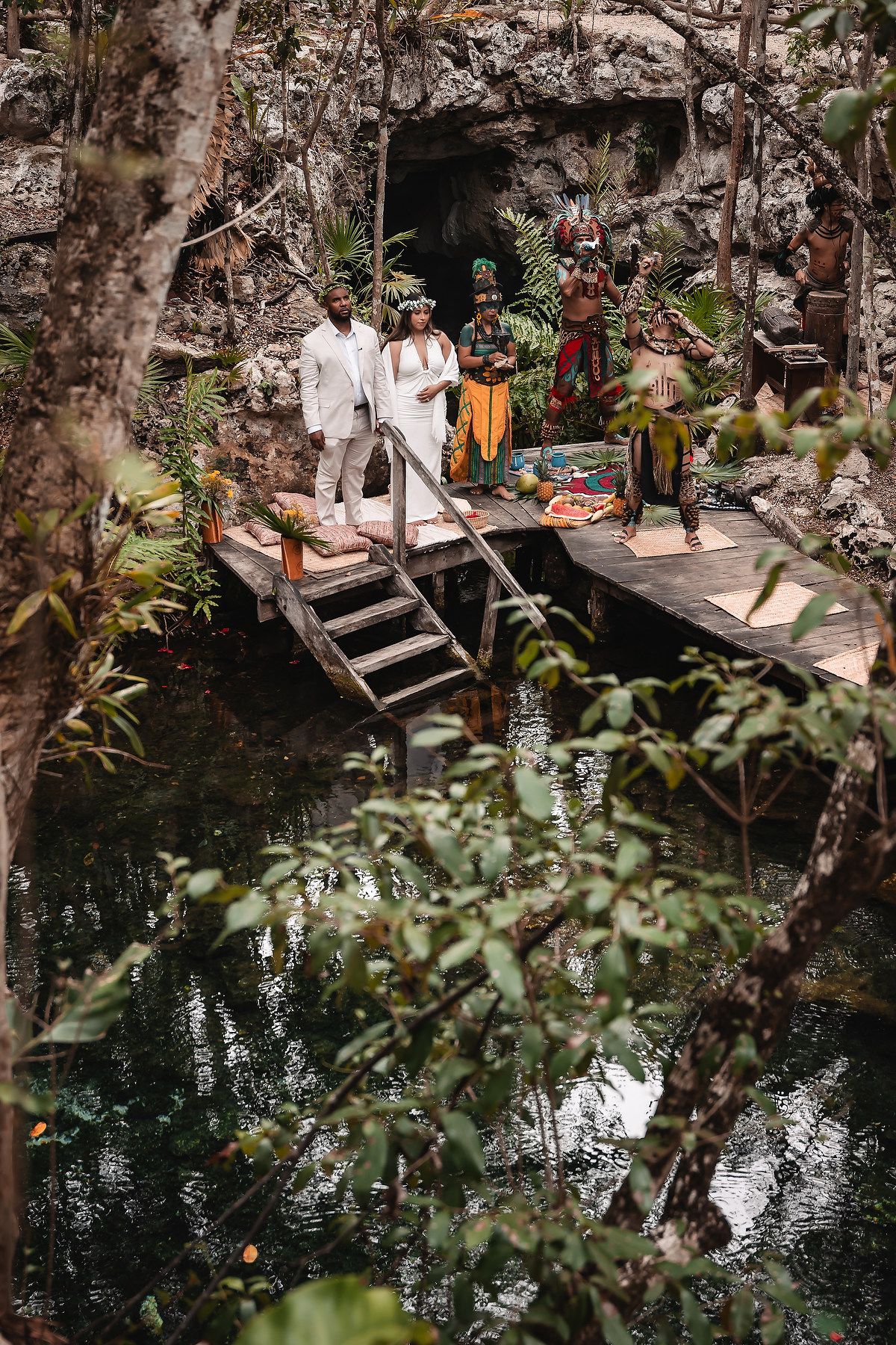 Traditional Mayan ceremony setup on wooden platform over crystal clear cenote waters.