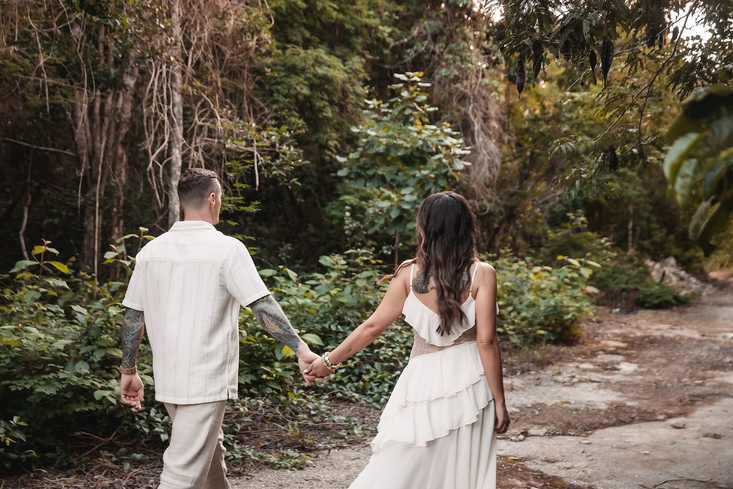 A romantic couple strolls hand in hand on a winding forest trail surrounded by fall foliage.