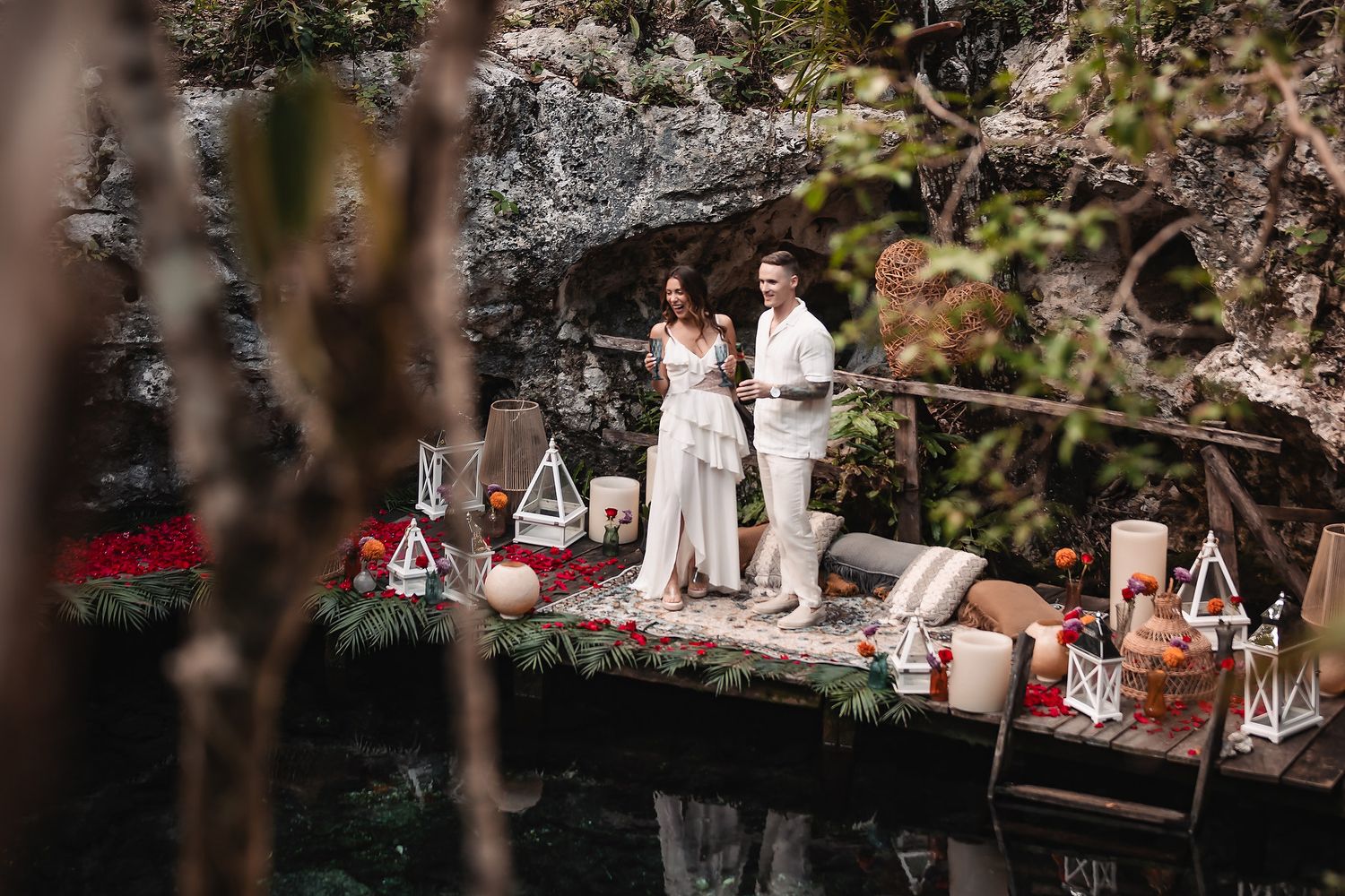 Elegant outdoor celebration setup with white decor and lanterns on a natural stone ledge.