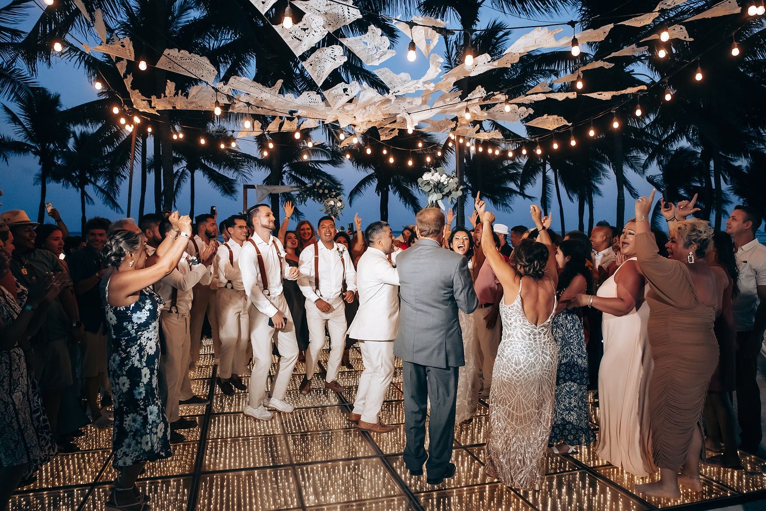 Wedding reception party with string lights overhead as guests dance and celebrate at night.