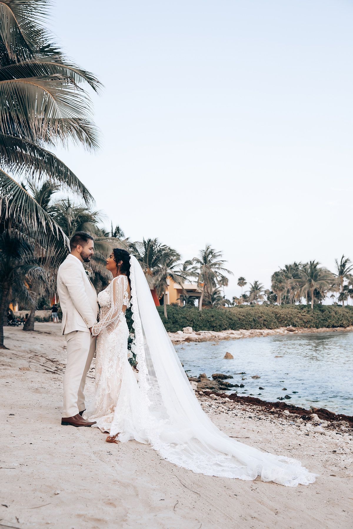 A romantic beach wedding photoshoot with palm trees and ocean waves in the background.